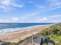 The property sits just steps from an expansive stretch of sandy coastline, where gentle waves roll in under a spacious blue sky.