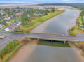 Aerial view of a coastal river winding through residential neighborhoods toward sandy beaches and ocean waters beyond.