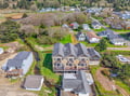 Aerial view of a large coastal vacation rental property nestled in a quiet residential neighborhood, surrounded by green spaces and nearby homes.