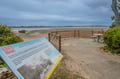 A scenic coastal heritage area with a wooden observation deck overlooking expansive sandy shores and calm waters, surrounded by native vegetation.
