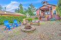 Charming red cabin exterior with welcoming front porch, surrounded by lush greenery and featuring a cozy gravel patio with fire pit and vibrant blue seating.