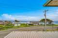 Oceanfront deck overlooking a coastal road, neighboring homes, and the rolling surf beyond. A peaceful arrival setting near the beach.