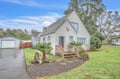Charming coastal cottage with blue trim sits among towering trees, featuring a welcoming front deck and mature landscaping in a peaceful residential setting.