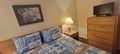 Settle into your comfortable bedroom featuring a cozy bed, warm bedside lamp, flat-screen TV, and coastal-inspired artwork that sets the perfect tone for your seaside escape.