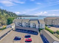 Aerial view of the property nestled along a scenic coastline, framed by lush forests and calm blue waters. Convenient parking and easy access to natural beauty all around.