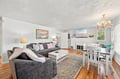 Settle into plush gray seating in your open-concept living space, where a charming chandelier casts warm light across gleaming hardwood floors. The cozy fireplace and dedicated dining nook invite relaxed evenings after exploring the area.