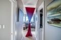 Step into your bright hallway where vibrant red curtains frame the welcoming living space ahead, complete with cozy seating and coastal artwork.