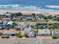 Aerial view of a charming beachside neighborhood where coastal homes nestle among lush greenery just steps from sandy shores and rolling waves.