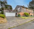 Charming coastal cottage surrounded by mature trees and greenery, offering a peaceful neighborhood setting with convenient parking and a spacious rooftop deck for relaxation.