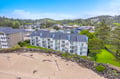Beachfront property nestled along a serene sandy shore, surrounded by lush green spaces and rolling forested hills.