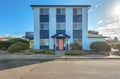 A distinctive blue three-story property featuring a welcoming coral-colored front entrance, set in a peaceful residential neighborhood with mature landscaping and sunny skies overhead.