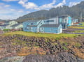 Charming coastal home nestled among colorful beach houses, with forested hills and natural rock formations creating a picturesque seaside setting.