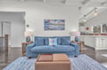 Sink into this plush blue sofa and unwind in your open-concept living space, where coastal art and warm lighting create the perfect atmosphere for relaxation.