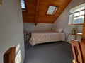 Unwind in your cozy attic retreat where skylights flood warm light across peaceful bedding and rustic beams create intimate charm.