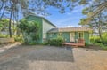 A charming green cottage nestled among tall pines, offering a peaceful retreat with a private gravel driveway and welcoming front deck—the perfect coastal escape.