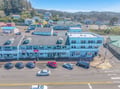 Aerial view of a charming coastal town featuring local shops, restaurants, and accommodations nestled between forested hills and community streets.