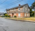 A charming two-story home featuring classic shingled upper level and brick foundation, nestled in a peaceful residential neighborhood with mature trees and a spacious fenced yard.