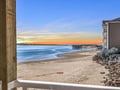A peaceful coastal sunrise over sandy shores, calm waters, and a nearby pier marks the start of a new day at this beachfront property.