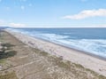 Expansive coastline stretches along pristine sandy shores with rolling waves meeting natural dunes and vegetation.