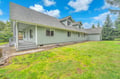 A charming green ranch-style home sits on spacious grounds surrounded by mature evergreen trees and open lawn areas.