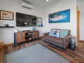 Unwind in your stylish living room featuring coastal artwork, leather sofa, and modern entertainment center—perfect for relaxing evenings.