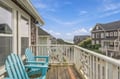 A private balcony offers two comfortable Adirondack chairs and a charming coastal neighborhood setting with ocean glimpses beyond the nearby homes.