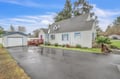 Charming single-story home with gray siding, blue trim, and covered front deck surrounded by mature trees and landscaping.