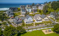 Aerial view of a charming coastal neighborhood with beach homes nestled among mature trees, just steps from the Pacific Ocean with ocean views and beach access nearby.