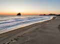 Pristine beach stretches along the coastline with dramatic rock formations rising from the ocean during golden hour.