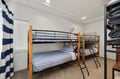 Your cozy bunk room offers comfortable sleeping for four with soft striped bedding and thoughtful storage shelves.
