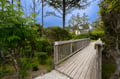Charming wooden boardwalk winds through lush landscaping beneath towering trees, creating a peaceful pathway to your retreat.