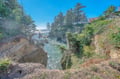 Dramatic coastal cliffs frame a secluded cove where ocean waves meet towering evergreens and rugged rock formations.