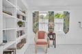 Curl up with your favorite book in this charming reading nook, where floor-to-ceiling shelves and a cozy coral chair create your perfect literary escape.
