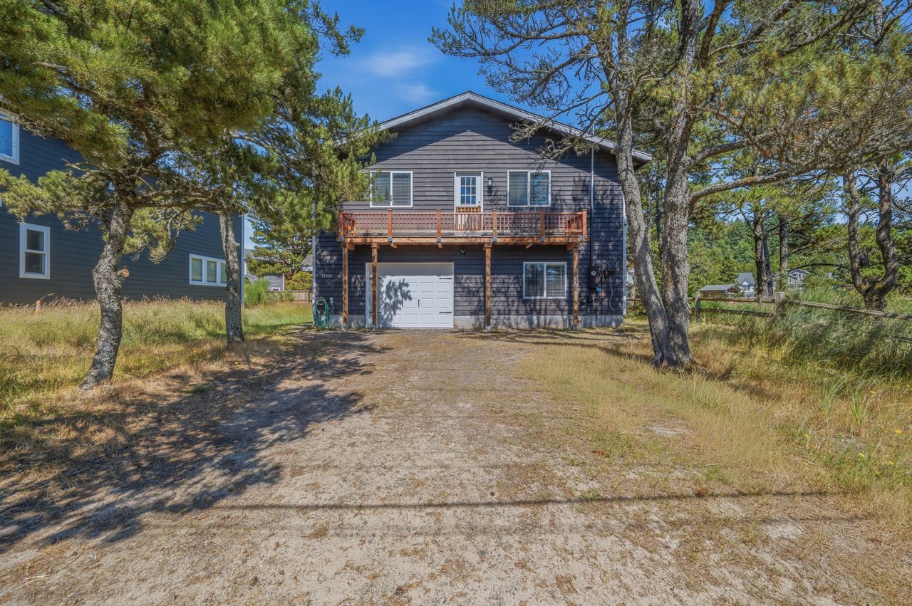 A coastal retreat nestled among windswept pines, with charming weathered-wood siding, a welcoming balcony, and convenient garage access in a tranquil natural setting.