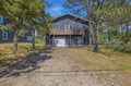 A coastal retreat nestled among windswept pines, with charming weathered-wood siding, a welcoming balcony, and convenient garage access in a tranquil natural setting.