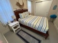 Relax in your cozy bedroom with coastal-striped bedding, natural light streaming through blinds, and thoughtful touches like beach decor.