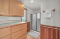 Warm wood cabinetry frames your private glass-enclosed shower, while fluffy towels await on bronze fixtures. Natural light streams in as you refresh.