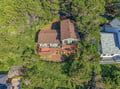 An aerial view reveals the property nestled among towering trees in a peaceful wooded setting, with a spacious deck perfect for outdoor relaxation.
