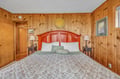Sink into the warmth of your rustic wood-paneled bedroom, where a rich cherry headboard and soft linens create your perfect mountain retreat.