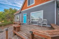 Welcoming property exterior featuring a spacious wooden deck and bright turquoise entrance door surrounded by mature trees.