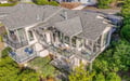 Modern vacation home with expansive outdoor decking and panoramic windows, surrounded by mature landscaping and neighboring properties.