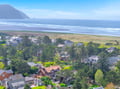 Aerial view of coastal neighborhood with tree-lined streets leading to pristine beach and dramatic mountain coastline.