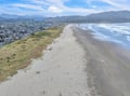 Aerial view captures the stunning coastline with expansive sandy beaches stretching along the scenic mountain-backed shoreline.