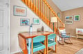 Settle into your cozy workspace with warm wood tones and cheerful turquoise chairs beneath charming local artwork.