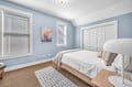 Drift into peaceful sleep in your serene blue bedroom, where soft natural light filters through blinds onto crisp white linens and warm carpeting.