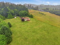Aerial view capturing the property nestled amid rolling meadows and forested hillsides, with mountain ridges defining the scenic horizon beyond.