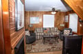 Picture yourself unwinding in this warm, wood-paneled living room with comfortable seating, natural light, and a ceiling fan for your comfort. The perfect retreat after exploring.