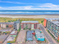 Aerial view of coastal accommodation buildings positioned just steps from the sandy beach and rolling ocean waves.