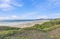 A stunning coastal stretch with soft sands and gentle surf, framed by lush greenery and rolling hills in the distance—a serene beachside setting nearby.