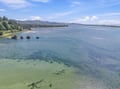 An aerial view captures the stunning coastal landscape surrounding the property, with pristine waters, sandy shoreline, forested hillsides, and distant mountains creating a scenic natural setting.